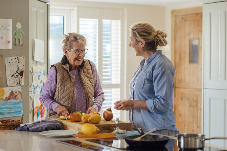 An older woman who made non-medical home care a component of her long-term care planning smiles as she and her caregiver prepare a meal together.